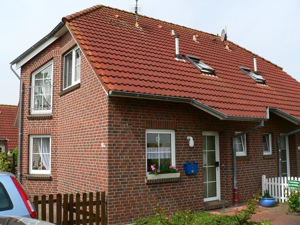 A two-story brick house with a red-tiled roof, a wooden fence, and a small garden area.