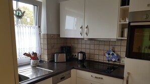 Une cuisine avec des meubles blancs, un plan de travail noir, un grille-pain, une bouilloire et une fenêtre avec un rideau.
