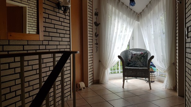 Une pièce avec un mur en briques, une porte en bois, une chaise en osier et un sol carrelé.