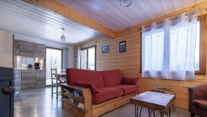 A cozy cabin interior with a wooden floor, a red sofa, a wooden coffee table, and a kitchen area visible through an open door. - Exceptional ski slopes superb chalet for 4 people 2 bedrooms 2 toilets (Gérardmer)