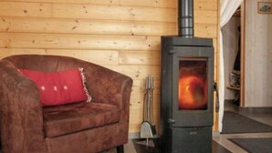 A cozy room with a wooden wall, a brown sofa with a red cushion, and a wood-burning stove. - Exceptional ski slopes superb chalet for 4 people 2 bedrooms 2 toilets (Gérardmer)