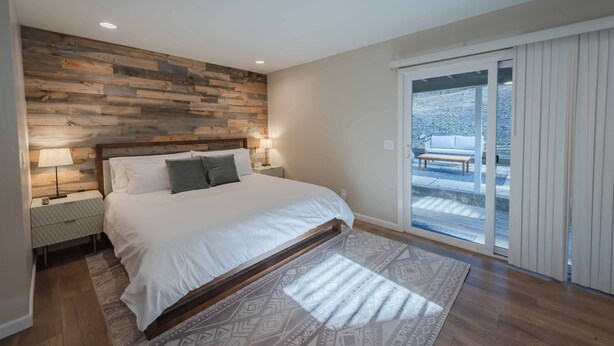 A bedroom with a wooden headboard, a large bed, bedside lamps, and a view of an outdoor patio through a sliding glass door.