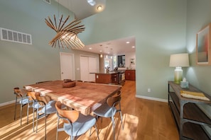 A spacious dining area with a large wooden table and modern chairs, a unique bamboo chandelier, and a view into the kitchen and living area. - 4BR/3BA Home Away from Home with Exceptional Amenities! (Atascadero)