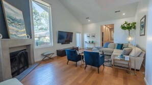 A modern living room with a fireplace, a flat-screen TV, a sofa, two blue armchairs, and a coffee table.