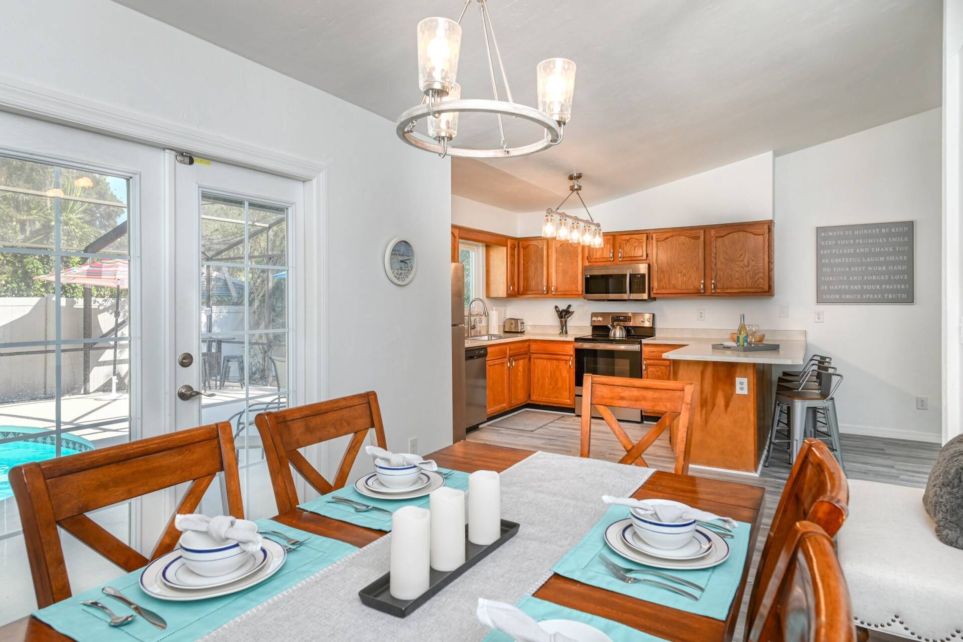 A dining area with a table set for four, a kitchen in the background, and a view of the outdoors.