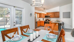 A dining area with a table set for four, a kitchen in the background, and a view of the outdoors. - River's Edge Retreat (St. Augustine)
