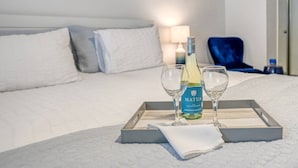 A neatly made bed with white linens and pillows, a bedside table with a lamp, and a tray with a bottle of wine and two glasses. - River's Edge Retreat (St. Augustine)
