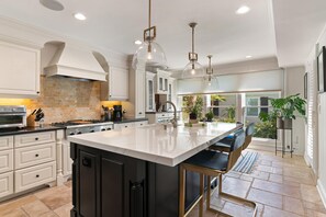 A spacious kitchen with a large island, white cabinetry, and modern pendant lighting.