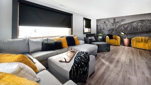 Un salon moderne avec un canapé gris, des fauteuils jaunes et une grande fenêtre dotée d’un store noir.