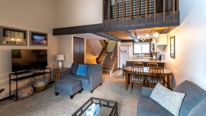 A spacious living room with a large TV, a sofa, a coffee table, and a dining area with chairs and a table. - Fraser 3BR Condo with Pool and Hot Tub (Fraser)