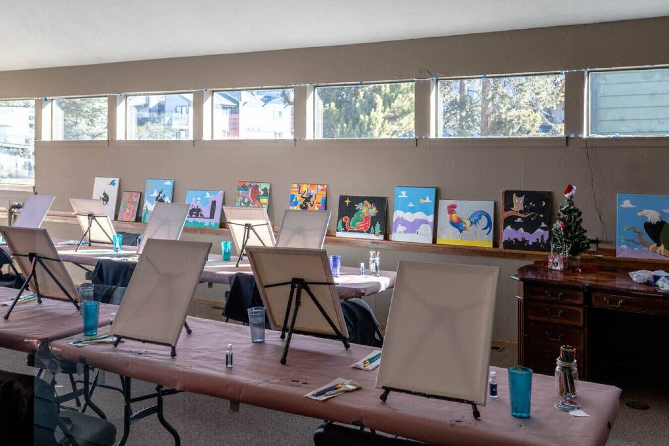 A room with multiple easels set up for painting, a wooden table, and a window with a view of trees.