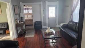 Una sala de estar con una mesa de centro de vidrio, un sofá de cuero negro, un sillón negro y un sofá color beige al fondo.