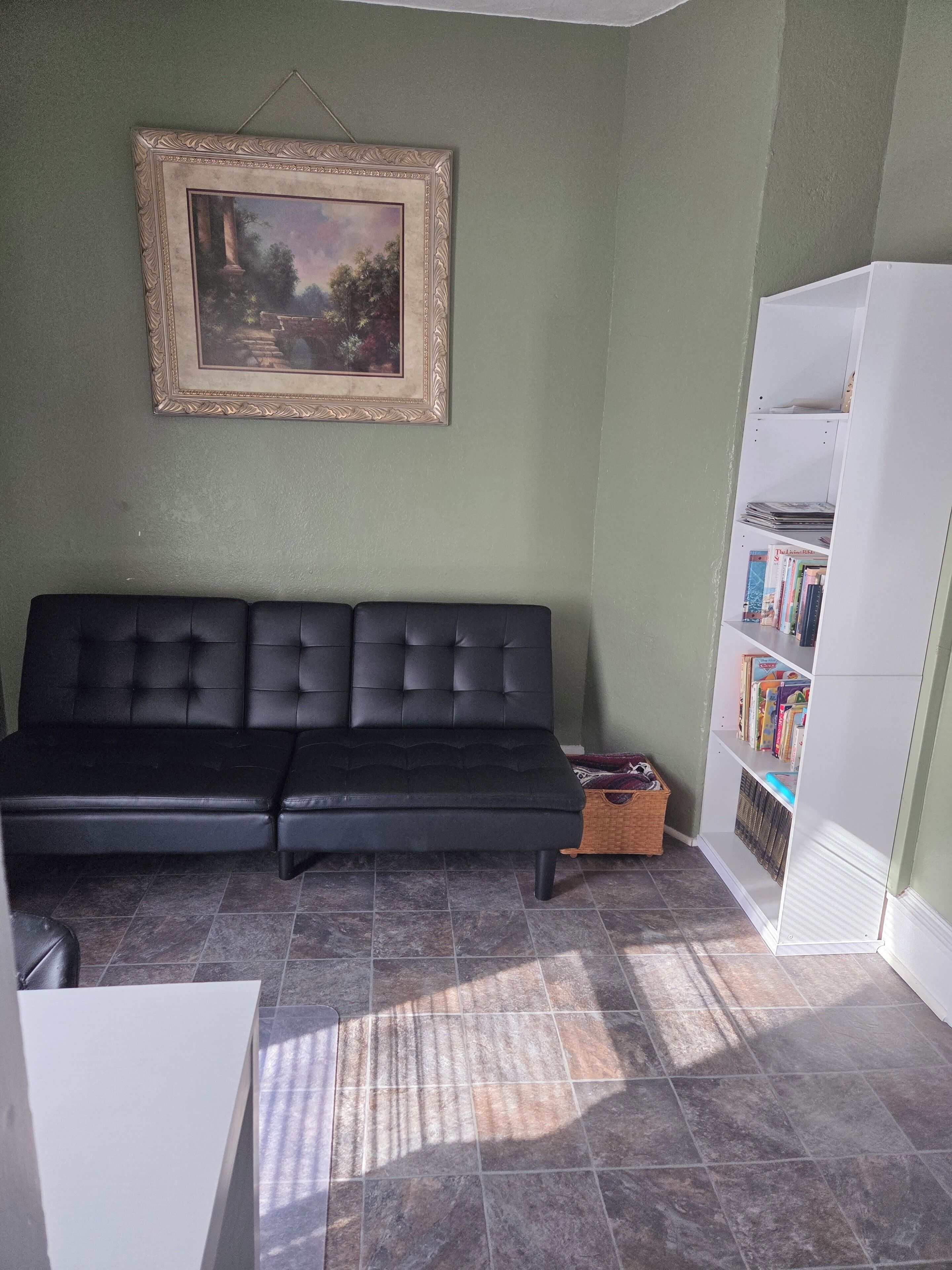A living room with a black sofa, a bookshelf, and a framed painting on the wall.