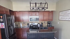 Una cocina moderna con armarios de madera oscura, un refrigerador de acero inoxidable, un microondas, una estufa y una cafetera. Hay dos taburetes de madera en la isla.