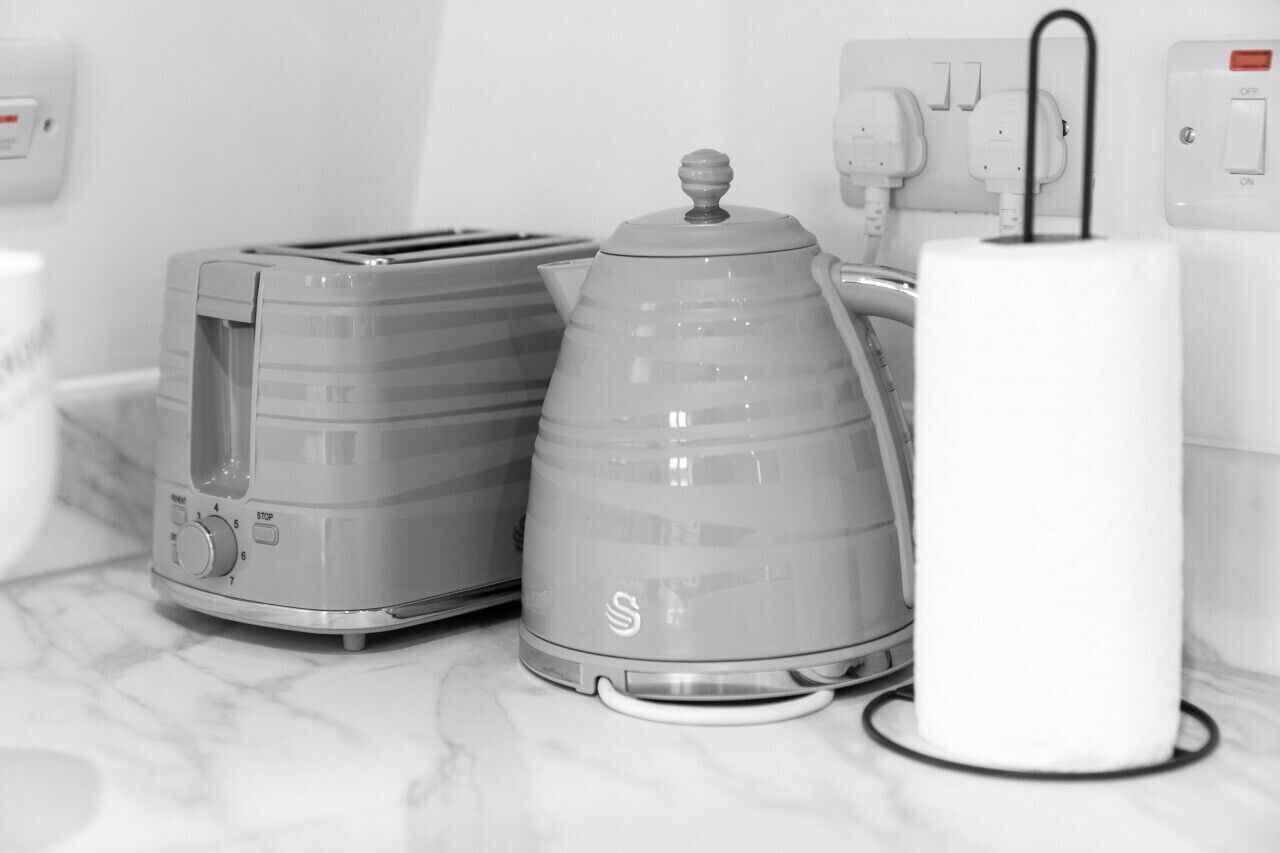 Uma cozinha com torradeira, chaleira e um objeto cilíndrico branco em uma bancada de mármore.