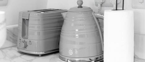 Uma cozinha com torradeira, chaleira e um objeto cilíndrico branco em uma bancada de mármore.