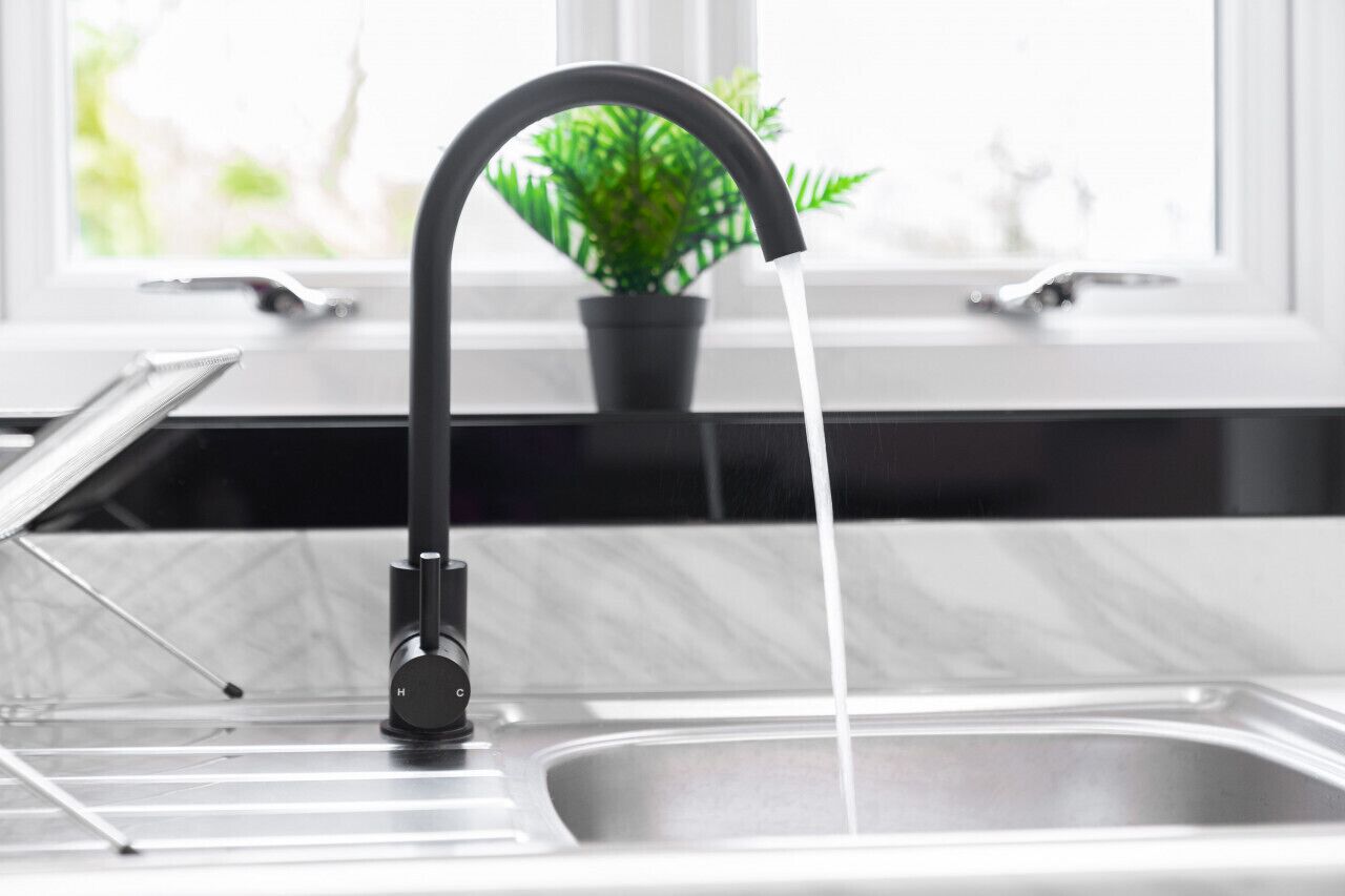 Eine moderne Küche mit einem eleganten schwarzen Wasserhahn, einer Marmorarbeitsplatte und einem Fenster mit Blick ins Grüne.