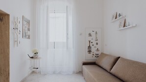 A minimalist living room with a white sofa, a small side table with a vase, and a door with nautical decorations.