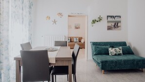 A modern living room with a dining area, a green sofa, and a view of the sea.