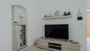 A modern living room with a flat-screen TV, wooden entertainment unit, decorative items, and a small shelf with plants.