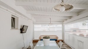 Una stanza con un tavolo con piano in vetro, una sedia in vimini, un divano e una ventola a soffitto.
