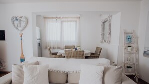 Una stanza accogliente con un divano bianco, un'area pranzo con sedie in vimini, uno scaffale a forma di cuore e una scala con lanterne.