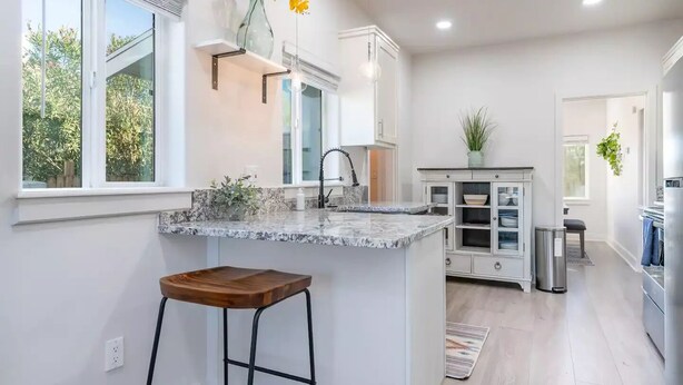 Una cocina moderna con encimera de mármol, un taburete de madera y un lavamanos integrado.