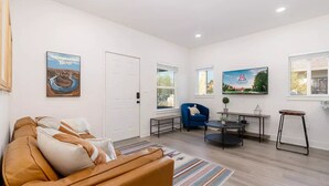 Una sala de estar moderna con un sofá, un sillón azul, una mesa de centro y un cuadro de un paisaje.