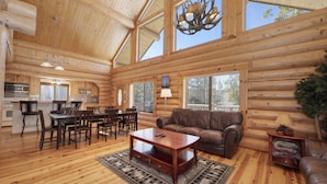 A spacious log cabin interior with a dining area, a living room with a sofa, and a kitchen. - Rocky Mountain cabin w/ fireplace & deck (Grand Lake)