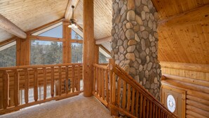 A wooden interior with a stone pillar, wooden railing, and a view through large windows. - Rocky Mountain cabin w/ fireplace & deck (Grand Lake)