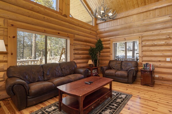 A log cabin interior with two leather sofas, a wooden coffee table, and a chandelier.