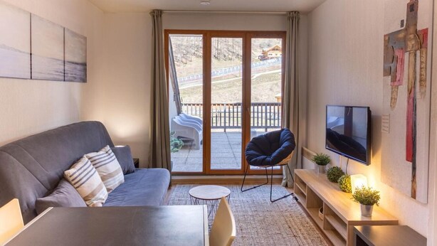 Una sala moderna con un sofá, una silla, un televisor y una pequeña mesa. Hay un ventanal corredero que da a un área exterior con un banco.