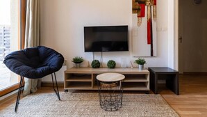 Una sala de estar moderna con un televisor de pantalla plana, una butaca negra, una mesita redonda y un adorno en la pared.