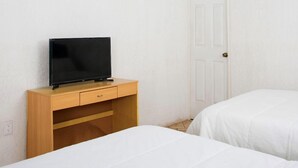Een slaapkamer met twee bedden, een plafondventilator, een televisie op een houten dressoir, en een witte deur.