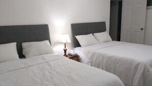 Een hotelkamer met twee bedden, witte beddengoed, een nachtkastje met een lamp en een deur.
