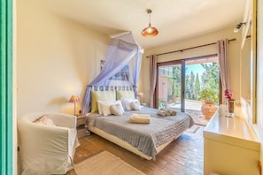 A bedroom with a bed, bedside table, lamp, and a view of the outdoors.