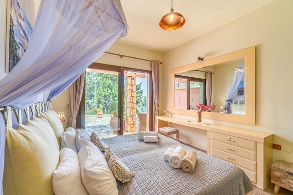 A bedroom with a bed, a large mirror, a vanity, and a view of the outdoors.