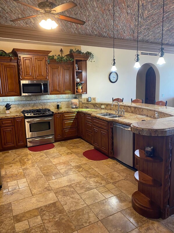 A kitchen with wooden cabinets, a stainless steel stove, a microwave, and a large island with a sink. - UPSCALE Beachfront Amazing 5 bedrooms. Pet Friendly! (Puerto Peñasco)