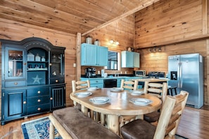 Ein Holzblockhaus-Innenraum mit einem Esstisch, gedeckt für sechs Personen, einer Küchenzeile mit blauen Schränken und einem großen Kühlschrank.