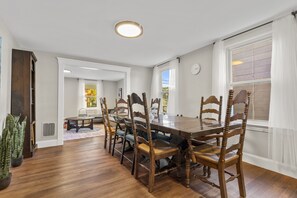 Une salle à manger avec une table et des chaises en bois, une plante en pot et une fenêtre avec des rideaux.
