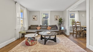 A modern living room with a sectional sofa, a round coffee table, and a dining area with a wooden table and chairs. - Modern 4 Bedroom Beach House: Ideal for Families & Long Stays (West Haven)