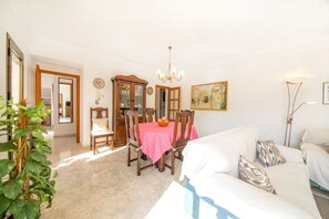 Een woonkamer met een eettafel, stoelen, een bank, een kroonluchter en een schilderij aan de muur.