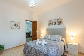 A bedroom with a bed, two bedside tables, a nightstand, and a door leading to another room.