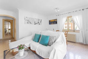 Un canapé blanc avec des coussins turquoise, une table basse en verre sur laquelle est posée une plante en pot, et des œuvres d’art accrochées au mur.