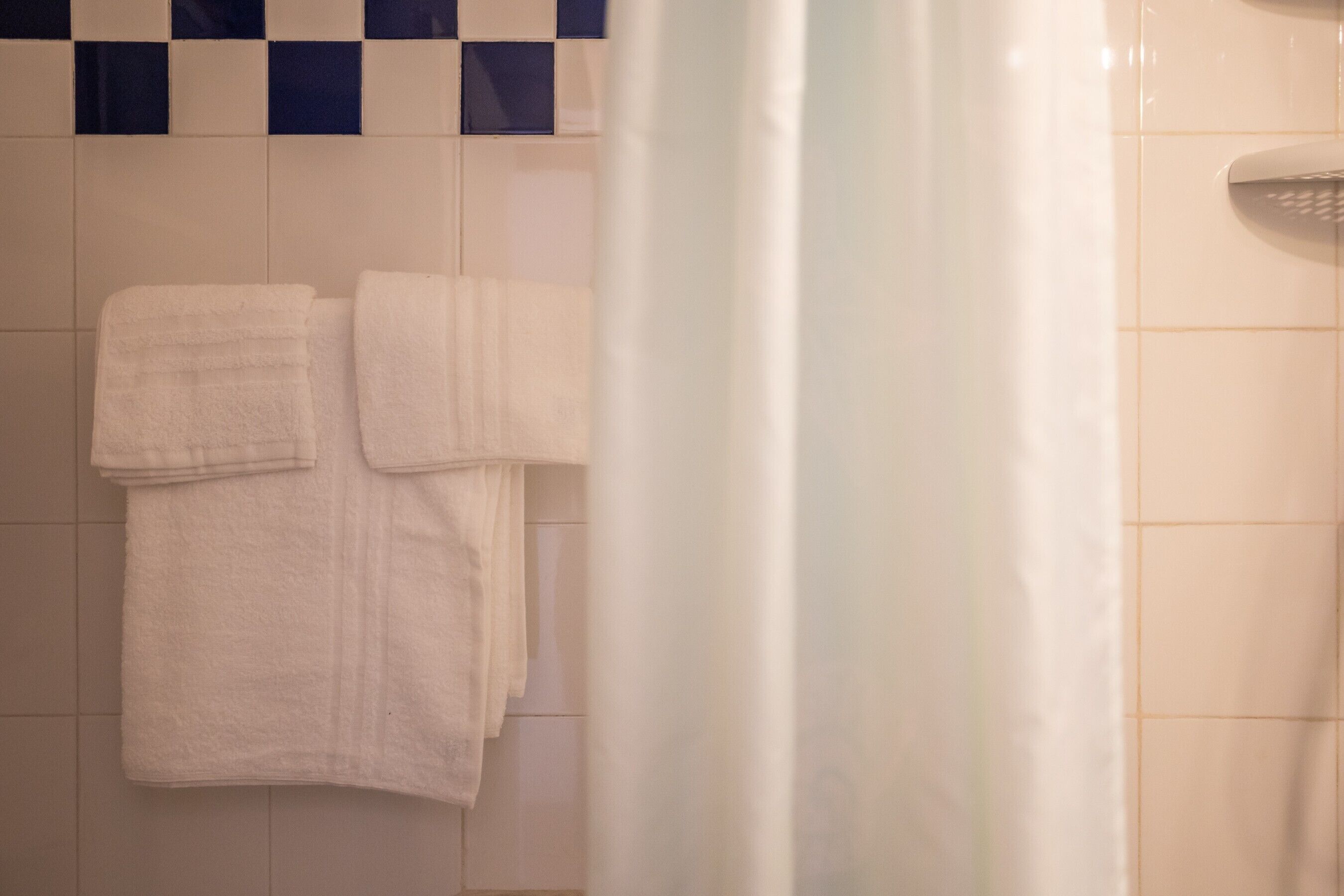 A bathroom with white tiled walls, a shower curtain, and two towels hanging on the wall.