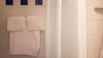 A bathroom with white tiled walls, a shower curtain, and two towels hanging on the wall.