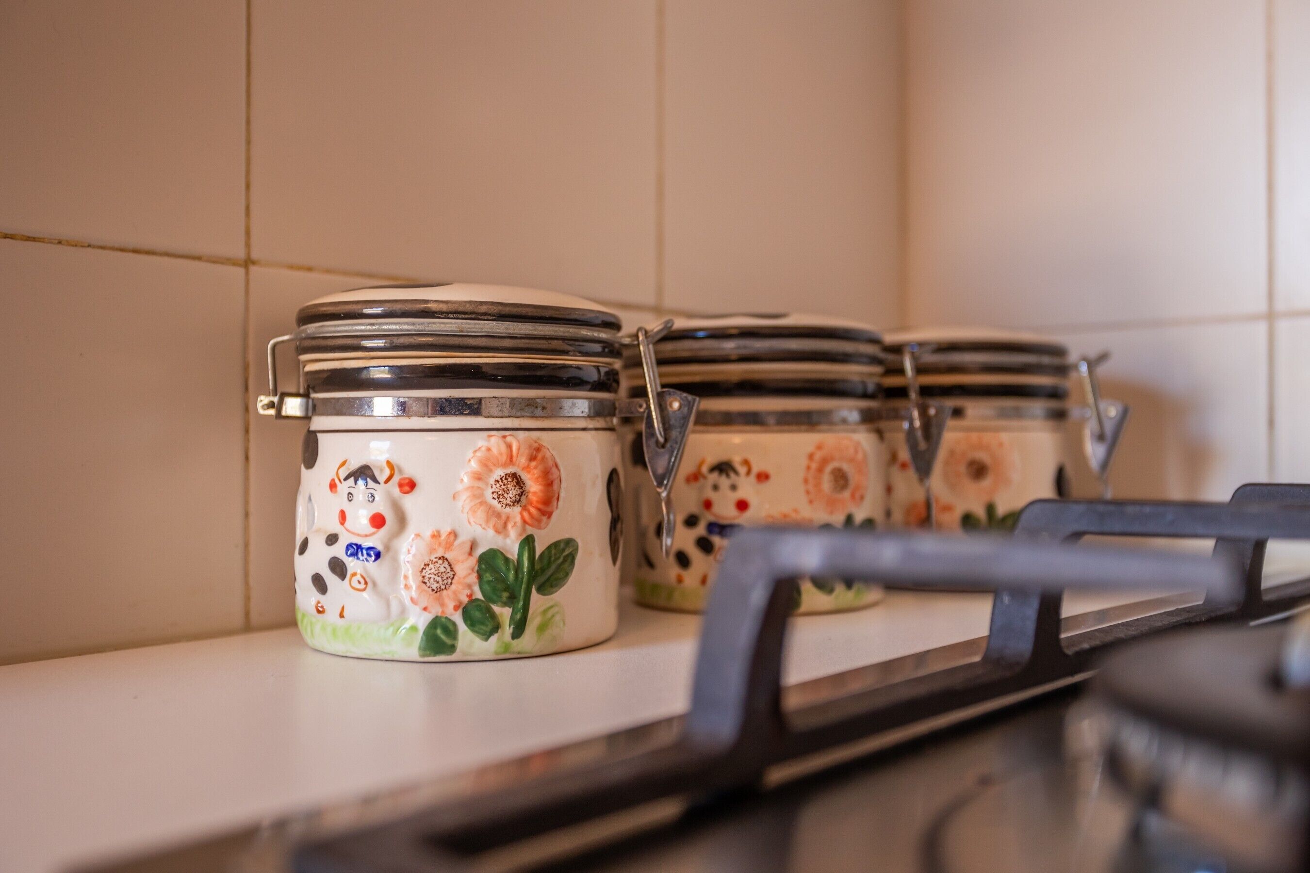 Potes de cerâmica com motivos florais numa prateleira de cozinha.