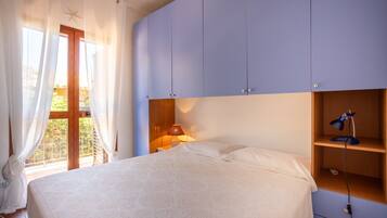 Ein Schlafzimmer mit Bett, Nachttisch mit Lampe, einer Holzablage und einem Fenster mit Vorhängen.