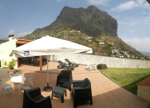 Un patio con mobiliario exterior, una sombrilla blanca y vistas a la montaña.