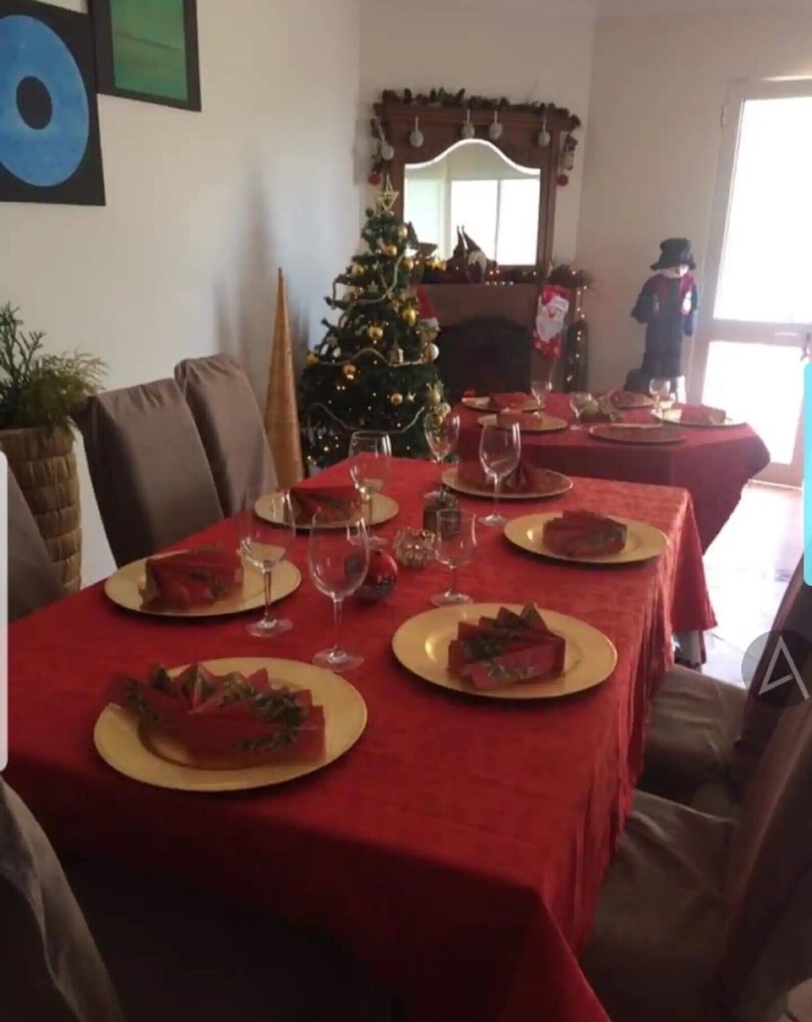 Ein Esszimmer mit Weihnachtsbaum, roten Tischdecken und Kamin.